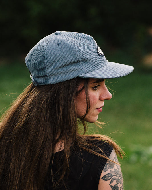 Woman wearing a blue FABRIC cap with a blurred natural background